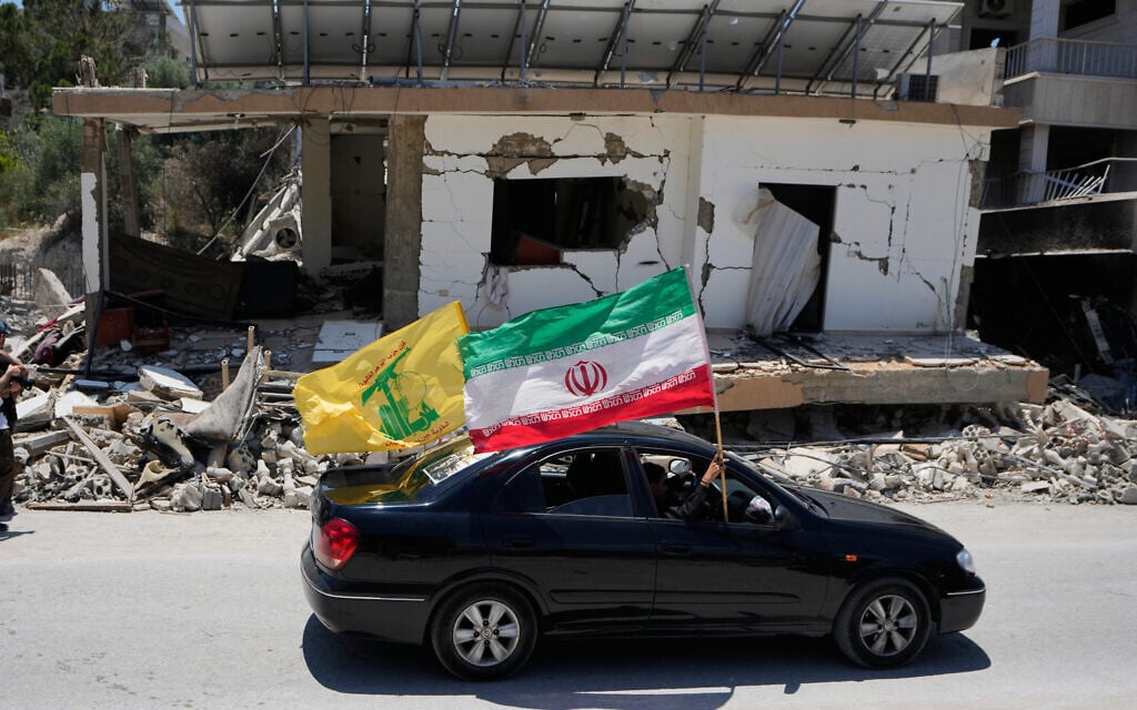Displaced people hold Iranian and Hezbollah flags as they drive by a building damaged in an Israeli airstrike in the southern Lebanon village of Chehabiyeh, June 16, 2026. (AP Photo/Mohammed Zaatari)