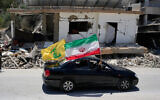 Displaced residents hold an Iranian and a Hezbollah flags as they pass by a destroyed building that was hit in a previous Israeli airstrike in the southern village of Chehabiyeh, Lebanon, June 16, 2026. (AP Photo/ Mohammed Zaatari)