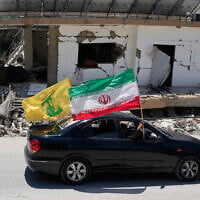 Displaced residents hold an Iranian and a Hezbollah flags as they pass by a destroyed building that was hit in a previous Israeli airstrike in the southern village of Chehabiyeh, Lebanon, June 16, 2026. (AP Photo/ Mohammed Zaatari)