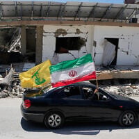 Displaced people hold Iranian and Hezbollah flags as they drive by a building damaged in an Israeli airstrike in the southern Lebanon village of Chehabiyeh, June 16, 2026. (AP Photo/Mohammed Zaatari)