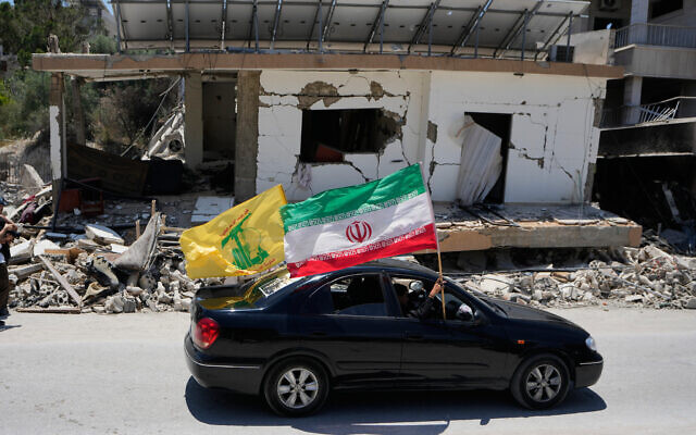 Displaced people hold Iranian and Hezbollah flags as they drive by a building damaged in an Israeli airstrike in the southern Lebanon village of Chehabiyeh, June 16, 2026. (AP Photo/Mohammed Zaatari)