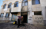 A man clears the rubble as writing in Hebrew on the wall reads 'revenge, regards to the arrested, people, wake up,' at one of the West Bank mosques that were vandalized and partly set on fire by Israeli settlers overnight, in the village of Jiljilya, north of Ramallah, June 17, 2026. (AP Photo/Majdi Mohammed)