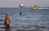 Residents swim in the waters of the Strait of Hormuz as a small motorboat passes cargo ships and other commercial vessels offshore near Bandar Abbas, Iran, June 17, 2026. (Amirhosein Khorgooi/ISNA via AP)