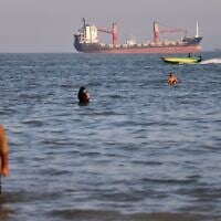 Residents swim in the waters of the Strait of Hormuz as a small motorboat passes cargo ships and other commercial vessels offshore near Bandar Abbas, Iran, June 17, 2026. (Amirhosein Khorgooi/ISNA via AP)