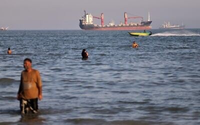 Residents swim in the waters of the Strait of Hormuz as a small motorboat passes cargo ships and other commercial vessels offshore near Bandar Abbas, Iran, June 17, 2026. (Amirhosein Khorgooi/ISNA via AP)