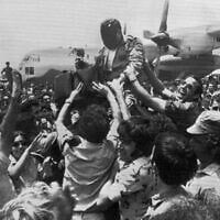 A cheering crowd at Ben-Gurion Airport raises a soldier in the rescue squad that freed the hijacked hostages from Uganda earlier in the day, July 4, 1976.  In the background is the C-130 transport plane which took part in the raid. The rescuer's face is obscured for security reasons. (AP Photo/Pool)