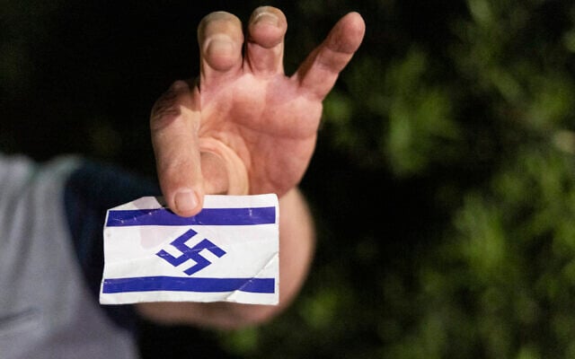 A man holds a sticker depicting a swastika during a protest against the jailing of yeshiva students who failed to comply with an army recruitment order, at the home of Supreme Court Deputy President Noam Sohlberg in Alon Shvut, June 3, 2026. (Chaim Goldberg/Flash90)