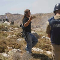 An Israeli settler records as security forces clash with Palestinians during a protest in Khirbet Humsa, west of Hebron in the West Bank, June 9, 2026. (Wisam Hashlamoun/Flash90)