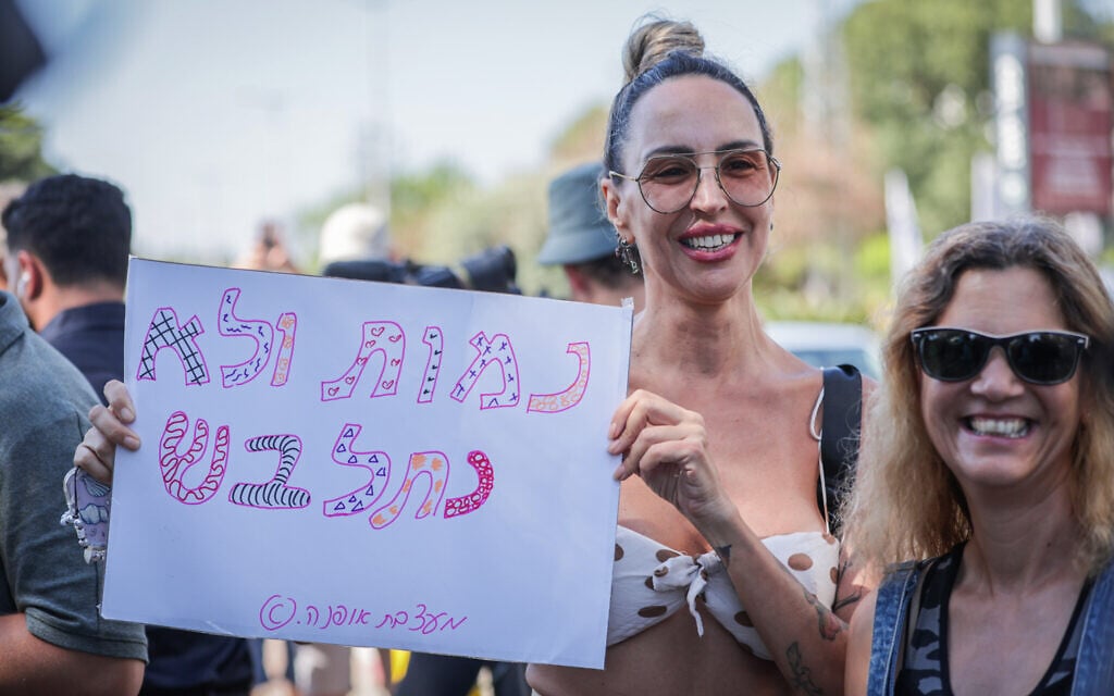 A resident of Kfar Yona holds a sign in Hebrew reading "We will die and not get dressed" -- a play on the popular ultra-Orthodox anti-conscription slogan "We will die and not enlist" -- at a counter-protest against a Haredi demonstration over the arrest of draft evaders near the Neve Tzedek (Beit Lid) military prison in the central Israel city, on June 24, 2026. (Tal Gal/Flash90)