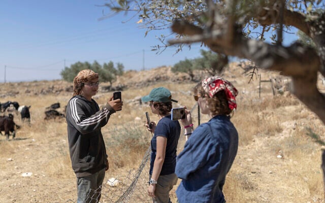 Protective presence activists (R) face off as they film using their mobile phones an Israel settler also filming them with his mobile phone, as he tries to enter the home of a Bedouin family in the West Bank, east of the Palestinian city of Ramallah, just outside the village of Taybeh on June 22, 2026. (ilia YEFIMOVICH / AFP)