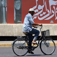 A cyclist rides past a billboard bearing pictures of Iran's late supreme leader Ayatollah Ali Khamenei, along a street in Baghdad on July 2, 2026, ahead of his funeral in Tehran. (Ahmad al-Rubate/AFP)