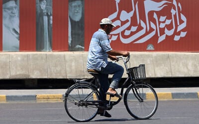 A cyclist rides past a billboard bearing pictures of Iran's late supreme leader Ayatollah Ali Khamenei, along a street in Baghdad on July 2, 2026, ahead of his funeral in Tehran. (Ahmad al-Rubate/AFP)
