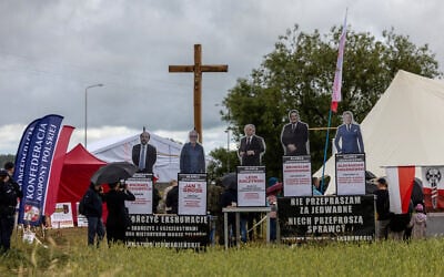 Banners reading 'I do not apologise for Jedwabne, let the perpetrators apologise' and 'Finish the exhumation, put an end to the slanders against Poles, the Jedwabne lie', with cut-out figures depicting Poland's Chief Rabbi Michael Schudrich and former Polish presidents are seen next to a crucifix set up at a gathering of far-right supporters who question the guilt of Polish citizens for the massacre in Jedwabne, on the sidelines of an official ceremony at the Jedwabne massacre monument honouring the memory of the town's Jewish residents murdered on July 10, 1941 by their Polish neighbours, in Jedwabne, north-eastern Poland, on July 10, 2026. (Photo by Wojtek RADWANSKI / AFP) Banners reading 'I do not apologise for Jedwabne, let the perpetrators apologise' and 'Finish the exhumation, put an end to the slanders against Poles, the Jedwabne lie', with cut-out figures depicting Poland's Chief Rabbi Michael Schudrich and former Polish presidents are seen next to a crucifix set up at a gathering of far-right supporters who question the guilt of Polish citizens for the massacre in Jedwabne, on the sidelines of an official ceremony at the Jedwabne massacre monument honouring the memory of the town's Jewish residents murdered on July 10, 1941 by their Polish neighbours, in Jedwabne, north-eastern Poland, on July 10, 2026. (Photo by Wojtek RADWANSKI / AFP)