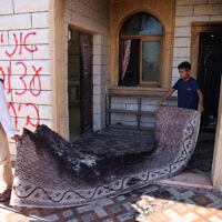 A Palestinian man and a child carry a burnt carpet out of a mosque whose entrance was torched and walls were daubed with Hebrew graffiti in an attack allegedly carried out by Israeli settlers in a Palestinian village near Hebron in the West Bank on July 19, 2026. (HAZEM BADER/AFP)