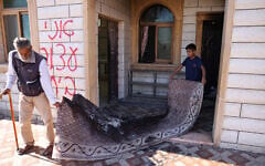 A Palestinian man and a child carry a burnt carpet out of a mosque whose entrance was torched and walls were daubed with Hebrew graffiti in an attack allegedly carried out by Israeli settlers in a Palestinian village near Hebron in the West Bank on July 19, 2026. (HAZEM BADER/AFP)