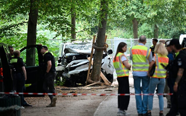 Police officers near the car that allegedly was driven into people killing one person and injuring 16 before crashing on a tree in the Tiergarten park on the outskirts of the Pride Parade in Berlin on July 26, 2026 (RALF HIRSCHBERGER/AFP)