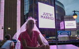 A Taylor Swift fan wearing a wedding veil sits at a restaurant next to New York's Madison Square Garden where a 'JUST&T MARRIED' sign is displayed during Taylor Swift's wedding with NFL star Travis Kelce on July 3, 2026. (AP Photo/Ryan Murphy)