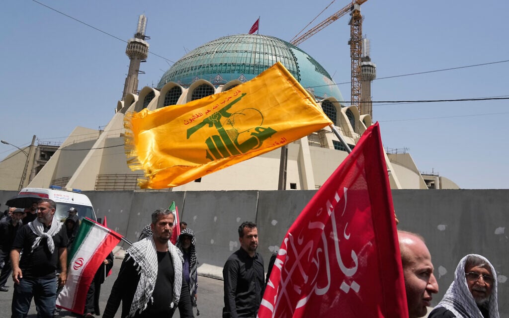 Mourners walk outside the Imam Khomeini Mosalla Grand Mosque as one carries a Hezbollah flag during the dayslong funeral ceremonies for the late Iranian Supreme Leader Ayatollah Ali Khamenei and members of his family in Tehran, Iran, July 4, 2026. (AP Photo/Vahid Salemi)