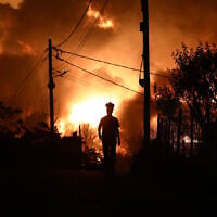 A man with a respirator mask on his head is silhouetted during a wildfire on the outskirts of the northern city of Thessaloniki, Greece, July 5, 2026. (AP Photo/Giannis Papanikos)