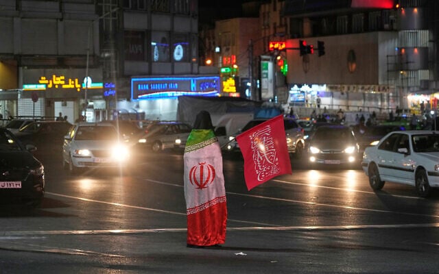 A pro-government demonstrator wears an Iranian flag as she holds a religious flag in a gathering commemorating the late Iranian Supreme Leader Ayatollah Ali Khamenei at a square in Tehran, Iran, July 11, 2026. (AP/Vahid Salemi)