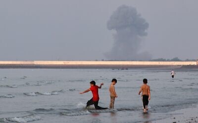 Three boys play in the shallow waters of the Strait of Hormuz, as a plume of smoke rises from an explosion in the background, off Bandar Abbas, Iran, July 13, 2026. (Razieh Poudat/ISNA via AP) Three boys play in the shallow waters of the Strait of Hormuz, as a plume of smoke rises from an explosion in the background, off Bandar Abbas, Iran, July 13, 2026. (Razieh Poudat/ISNA via AP)