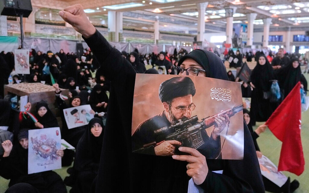 A mourner chants slogan as she holds a poster with graphic depicting Iran’s Supreme Leader Ayatollah Mojtaba Khamenei in a ceremony commemorating his father, the late supreme leader ayatollah Ali Khamenei at the Imam Khomeini Mosalla Grand Mosque in Tehran, July 14, 2026. (AP/Vahid Salemi)
