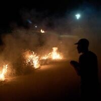 A Palestinian stands next to a fire after brush was set ablaze on the roadside to prevent an Israeli settler attack in the West Bank village of Sinjil, July 17, 2026. (AP/Leo Correa)