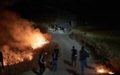 Israeli settlers, top, and Palestinians clash as brush burns along a roadside after Palestinians set it ablaze to prevent the settlers from approaching the West Bank village of Sinjil, July 17, 2026. (AP Photo/Leo Correa)