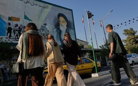 People cross the Islamic Revolution Street under a mural depicting a portrait of the Islamic Republic founder Ruhollah Khomeini in downtown Tehran, Iran, July 18, 2026. (AP Photo/Vahid Salemi)