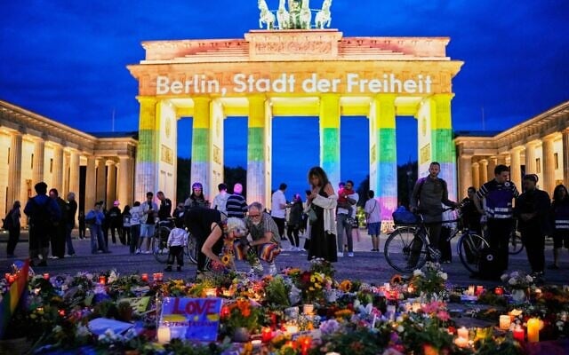 People gather in front of the Brandenburg Gate illuminated with the message 'Berlin, city of freedom,' commemorating victims after a car rammed into a crowd at the Pride March in Berlin, July 26, 2026. (AP Photo/ Ebrahim Noroozi)