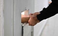 A guard grasps the hands of a cuffed prisoner through a door slot at the Givon Prison in Ramle on January 11, 2026. (Oren Cohen/Flash90)