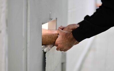 A guard grasps the hands of a cuffed prisoner through a door slot at the Givon Prison in Ramle on January 11, 2026. (Oren Cohen/Flash90) A guard grasps the hands of a cuffed prisoner through a door slot at the Givon Prison in Ramle on January 11, 2026. (Oren Cohen/Flash90)