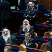 Prime Minister Benjamin Netanyahu (foreground) walks past ultra-Orthodox MKs as the Knesset prepares to pass a law banning the arrests of draft dodgers that will effectively freeze ultra-Orthodox enlistment into the IDF for at least the next seven months, July 14, 2026. Netanyahu left the chamber before the vote itself. At center, with hands around his mouth, is UTJ MK Meir Porush. (Chaim Goldberg/Flash90)