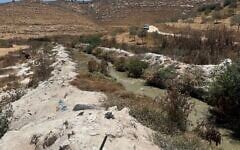 Contaminated water flows in the Hebron Stream below Palestinian village of ad-Dahariya, between banks coated in stone dust, July 14, 2026. (Sue Surkes/Times of Israel)