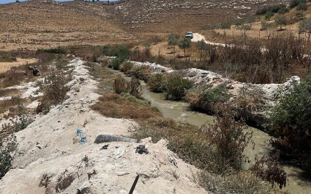 Contaminated water flows in the Hebron Stream below Palestinian village of ad-Dahariya, between banks coated in stone dust, July 14, 2026. (Sue Surkes/Times of Israel)