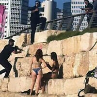 A member of Prime Minister Benjamin Netanyahu's security detail seen with his gun drawn near beachgoers as his team clears the area ahead of the premier's arrival to Charles Clore Beach, to film a video hailing the finding of the Altalena cargo ship, August 24, 2026. (Social media, used in accordance with Clause 27a of the Copyright Law)