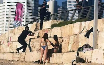 A member of Prime Minister Benjamin Netanyahu's security detail seen with his gun drawn near beachgoers as his team clears the area ahead of the premier's arrival to Charles Clore Beach, to film a video hailing the finding of the Altalena cargo ship, August 24, 2026. (Social media, used in accordance with Clause 27a of the Copyright Law)