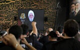 People react as Hezbollah Secretary-General Sheikh Naim Qassem addresses crowds via a screen during the first day of Ashura commemorations at the mausoleum of former Hezbollah leader Hassan Nasrallah in Beirut’s southern suburbs on June 17, 2026. (Anwar Amro/AFP)