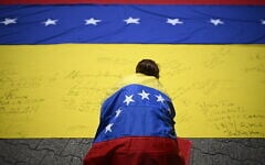 Illustrative: A unionist wrapped in a Venezuelan national flag, signs another Venezuelan national flag during a march in Caracas on July 28, 2026. (Federico PARRA/AFP)