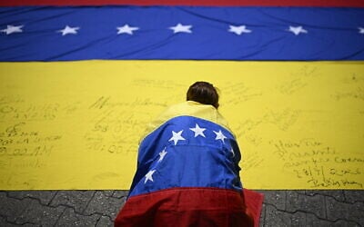 Illustrative: A unionist wrapped in a Venezuelan national flag, signs another Venezuelan national flag during a march in Caracas on July 28, 2026. (Federico PARRA/AFP) Illustrative: A unionist wrapped in a Venezuelan national flag, signs another Venezuelan national flag during a march in Caracas on July 28, 2026. (Federico PARRA/AFP)