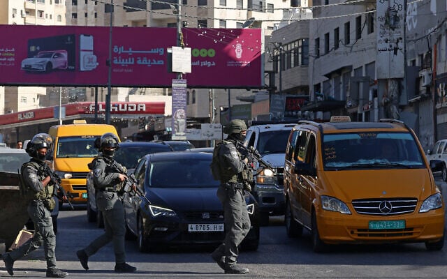Members of Israeli security forces patrol along a busy street during a military raid in the Qalandia refugee camp, south of Ramallah in the West Bank, August 5, 2026. (Zain JAAFAR/AFP)