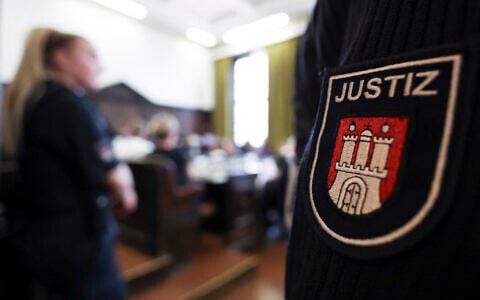 A logo on the uniform of a justice official is pictured as the defendants sit in the courtroom of the criminal justice building at the start of another day of hearings in the trial against the far-right terrorist group 'Last Wave of Defense,' on August 5, 2026 in Hamburg. (Christian Charisius/POOL/AFP)