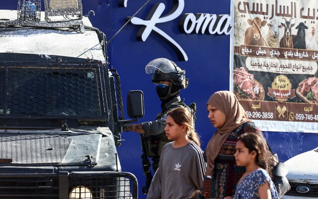 Palestinians walk past Israeli security forces deployed on a street during a military raid in the Qalandiya refugee camp, south of Ramallah in the West Bank, on August 5, 2026. (Zain JAAFAR/AFP)