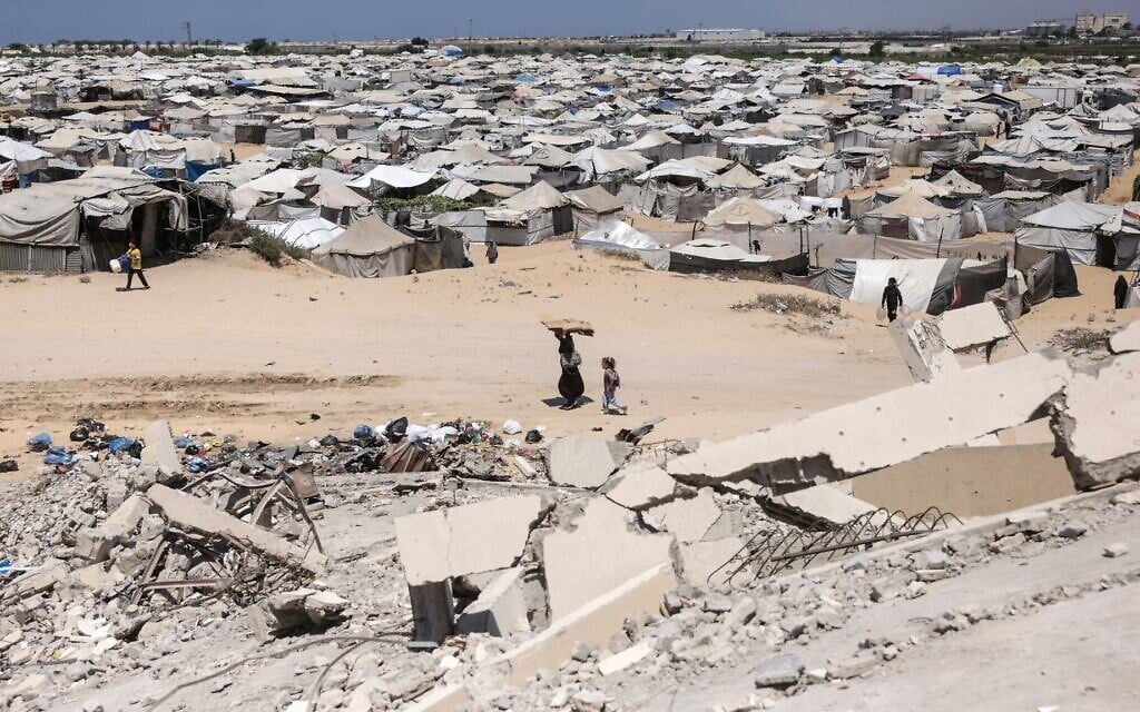 Palestinians walk past the rubble of buildings destroyed by the Israeli military, and hundreds of tents now housing them, in Khan Younis, southern Gaza Strip, on August 11, 2026. (Bashar Taleb/AFP)