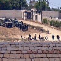 Israeli soldiers stand guard next to settlers (front) in front of the Palestinian houses in the village of Qusra, south of Nablus, in the West Bank, on August 12, 2026. (Zain Jaafar/AFP)