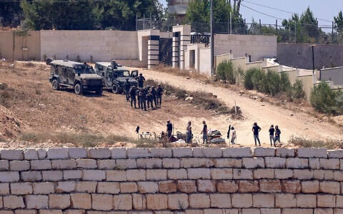 Israeli soldiers stand guard next to settlers (front) in front of the Palestinian houses in the village of Qusra, south of Nablus, in the West Bank, on August 12, 2026. (Zain Jaafar/AFP)