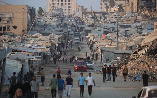Palestinians walk past tents and destroyed buildings near the beach front in Gaza City on August 14, 2026. (Eyad Baba/AFP)