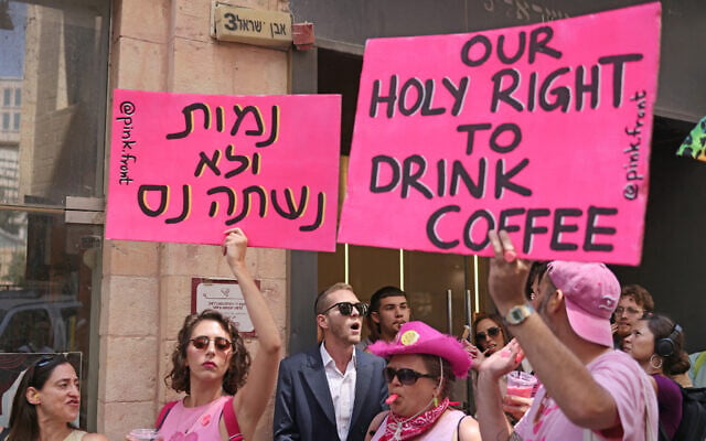 Secular activists hold up placards as they stage a counter-protest against Haredi men at Cafe Basimta in Jerusalem, on August 15, 2026. The Hebrew sign reads "We will die rather than drink instant," a play on a slogan used by Haredi men against the IDF draft. (AHMAD GHARABLI/AFP)