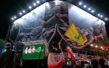 A demonstrator draped in an Iranian flag waves the flag of Iran's Lebanese proxy Hezbollah in front of a billboard that depicts US aircraft falling into Iranian forces' fishing nets, alongside the Persian caption, 'The Strait of Hormuz will remain closed; the entire Persian Gulf is our hunting ground,' during a pro-government rally at the Islamic Revolution Square in Tehran, Iran, on May 4, 2026. (AP Photo/Vahid Salemi)