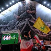 A demonstrator draped in an Iranian flag waves the flag of Iran's Lebanese proxy Hezbollah in front of a billboard that depicts US aircraft falling into Iranian forces' fishing nets, alongside the Persian caption, 'The Strait of Hormuz will remain closed; the entire Persian Gulf is our hunting ground,' during a pro-government rally at the Islamic Revolution Square in Tehran, Iran, on May 4, 2026. (AP Photo/Vahid Salemi)